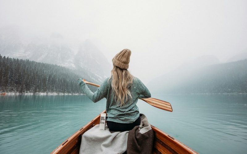 woman in gray long sleeve shirt sitting on brown wooden boat on body of water during